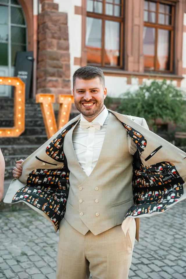 Bräutigam zeigt das Sakkofutter mit Bierflaschen-Muster, Hochzeit auf dem Schlossgut Lüll