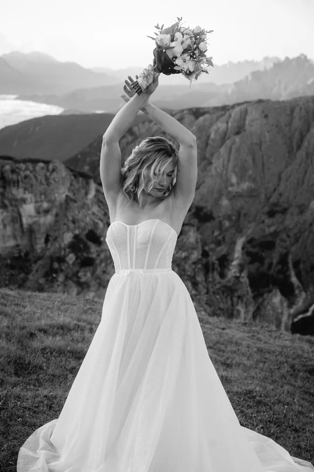 Braut hebt den Brautstrauß in die Luft, schwarz-weiß, After-Wedding-Shooting in den Dolomiten