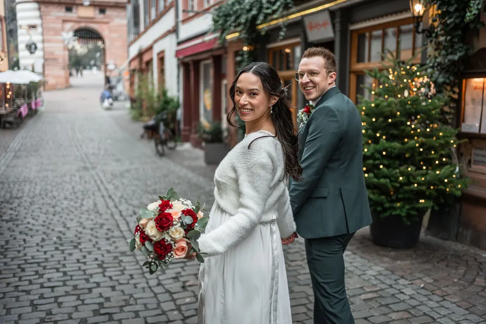 Kim und Jens lachen in die Kamera, neben ihnen ein Weihnachtsbaum vor einem Laden in der Steingasse, Brautpaarshooting in Heidelberg