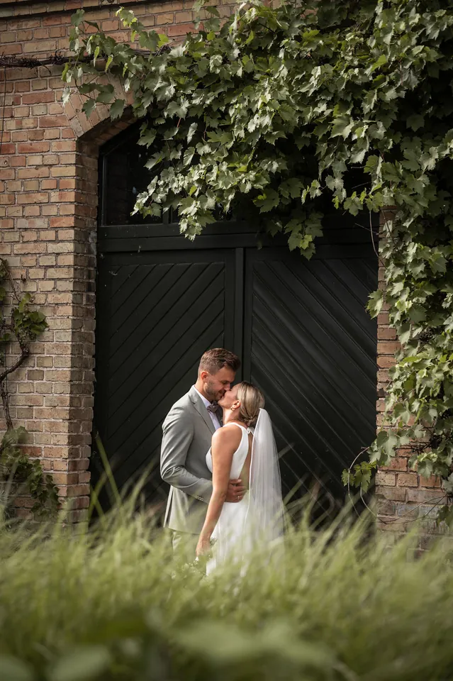 Kuss vor dem dunklen Scheunentor im hohen Gras, Hochzeit im Eichenstolz Ladenburg