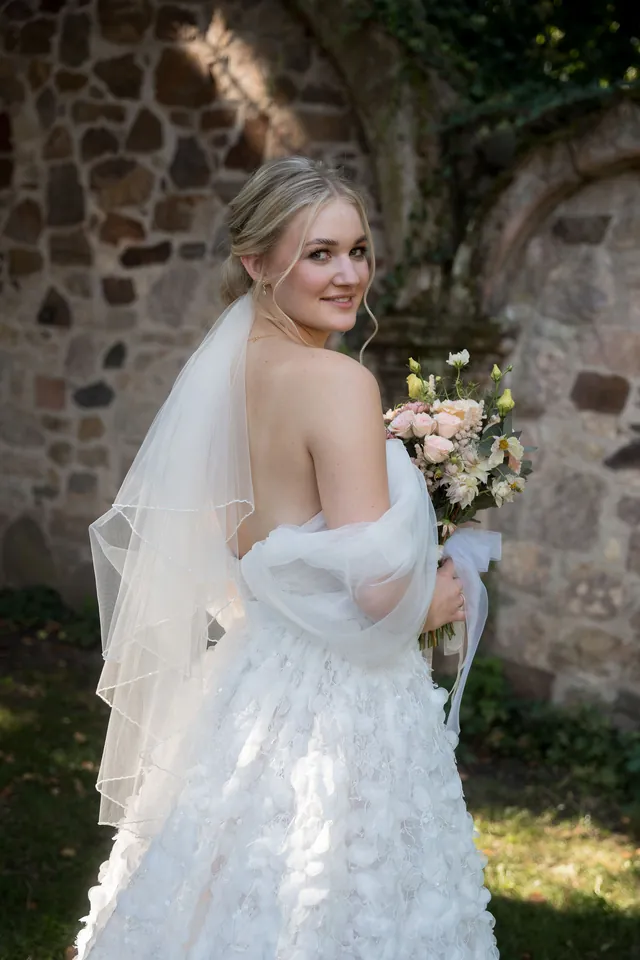 Braut blickt über die Schulter vor der alten Steinmauer, Hochzeit am Schloss Schwetzingen